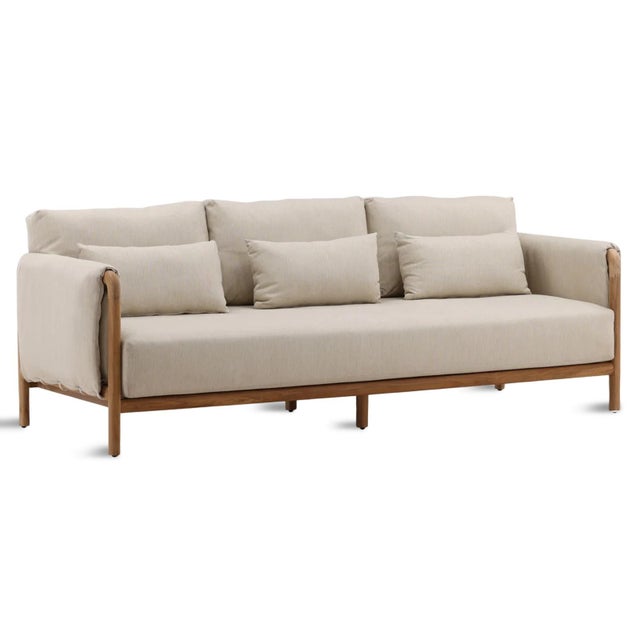 Teak frame outdoor sofa with beige upholstered cushions and accent pillows. Each sofa may vary in exact coloring, wood...