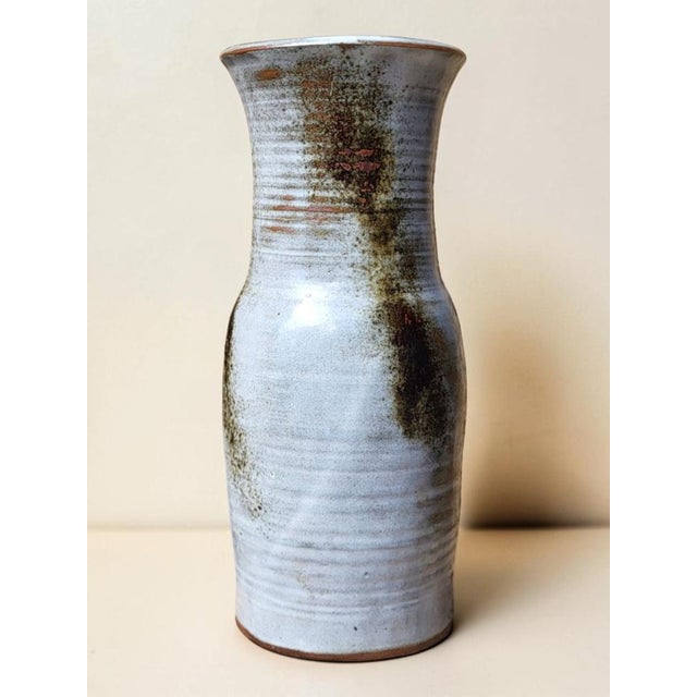 A glazed stoneware vase by Chantal and Robert Thierry, with a slender baluster shape, a narrow neck, and a wide, flared...