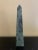 A beautifully proportioned marble obelisk in richly veined shades of green, cream, and grey. The sculptural silhouette and...