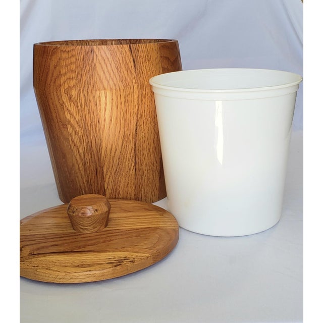 This is a vintage Mid-Century Modern (MCM) solid oak wooden ice bucket with a natural grain finish and a protective white...