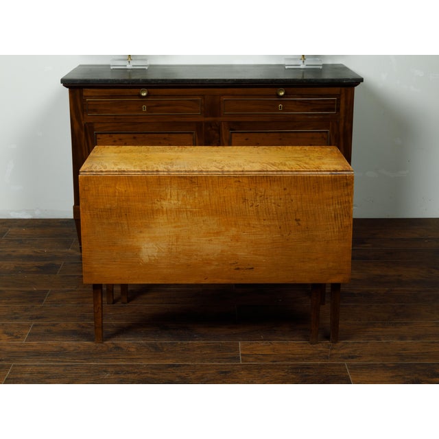 An American maple drop-leaf table from the 19th century, with tapered legs. Made in the USA during the 19th century, this...