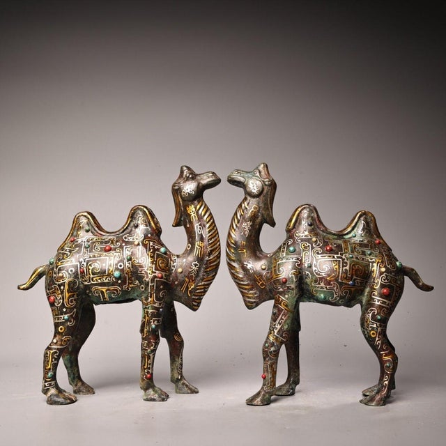 This is a matching pair of cast bronze Bactrian camel figurines, featuring extensive gold and silver inlay decoration....