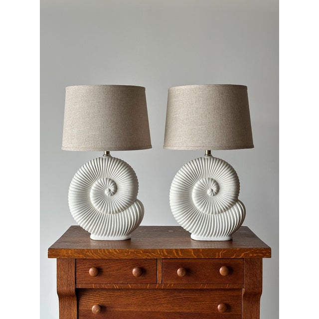 A pair of sculptural table lamps with nautilus shell-form plaster bases, each featuring a deeply ridged spiral design in a...