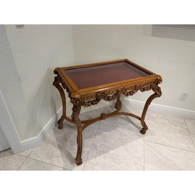 Finely carved walnut display table with a glass top set within a molded frame, over an apron richly decorated with floral...