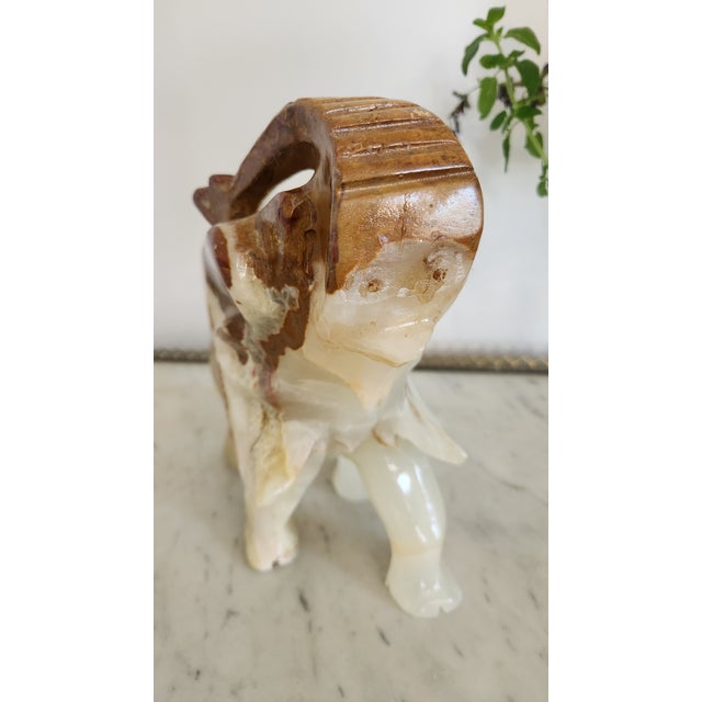 A large vintage carved onyx elephant sculpture featuring a raised trunk and beautifully varied cream, honey, amber, rust,...