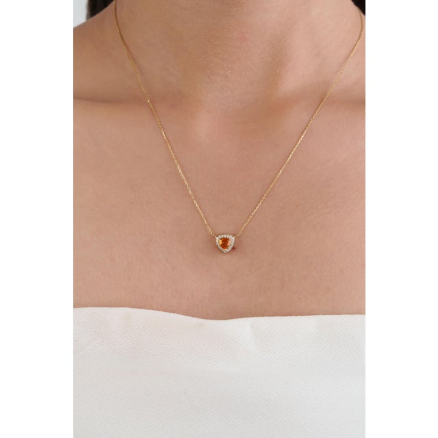 This elegant pendant necklace showcases a 0.53 carat natural trillion-cut orange sapphire, set in 14K yellow gold. The...
