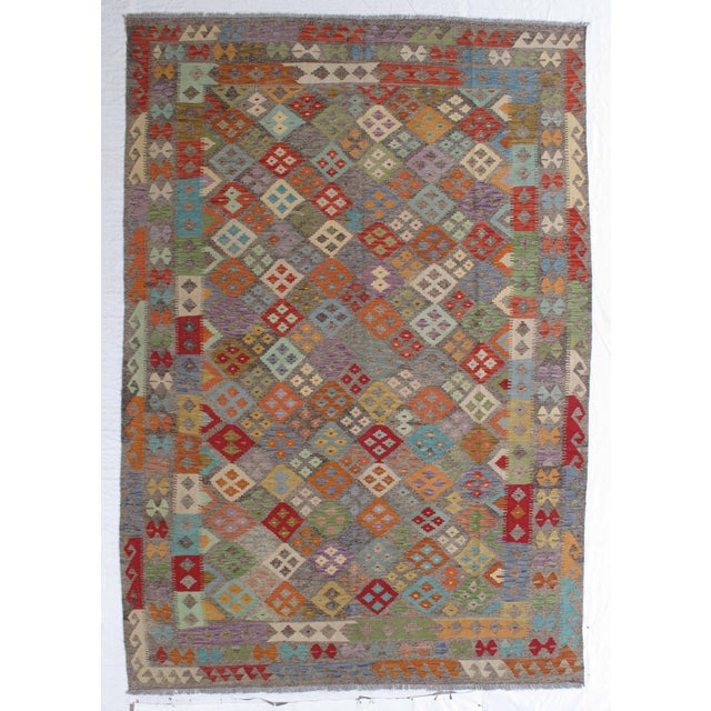 Handwoven Afghan kilim flatweave rug featuring an allover geometric diamond pattern in soft, muted multicolor tones. Woven...