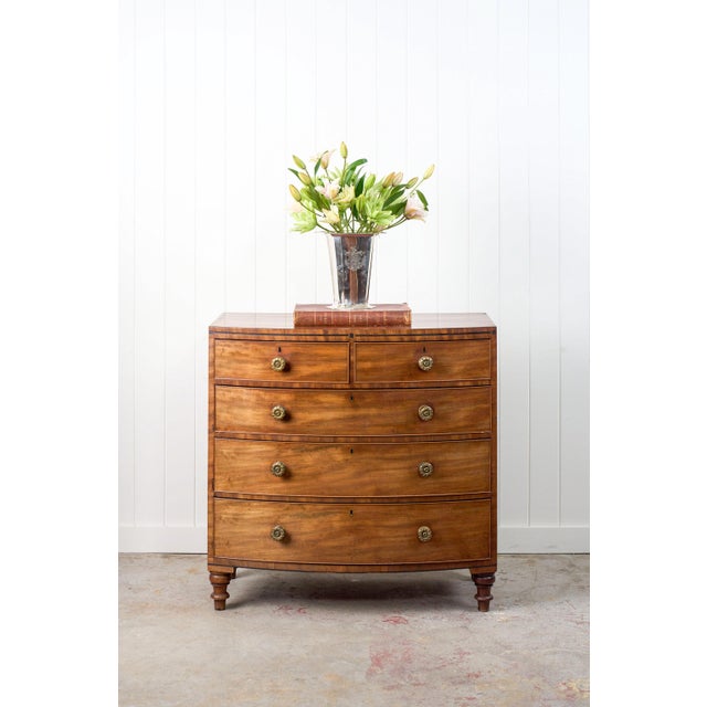 This George III period mahogany chest, circa 1820, features warm-toned mahogany and a bowed front. It includes five...
