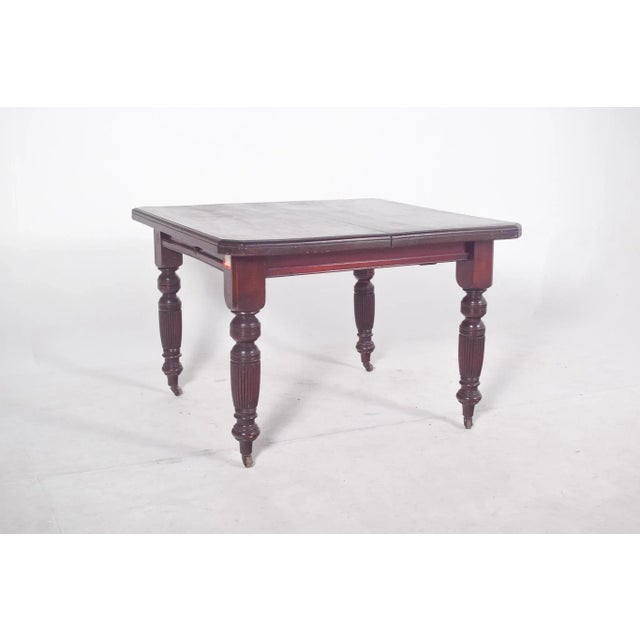 English dining table. It has a square top with slightly jagged edges, a smooth surface and a darkened finish. It rests on...
