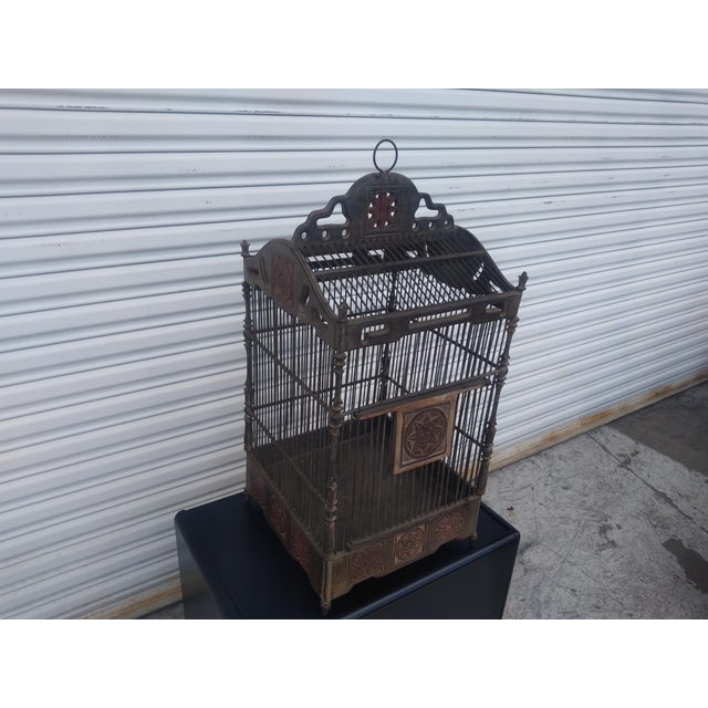 This is a stunning bird cage! It's made of metal and wood. It has a lot of intricate and finely detailed facets. The cage...