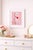 A pink ceramic poodle with a red heart is photographed against a soft pink background, creating a playful monochrome still...
