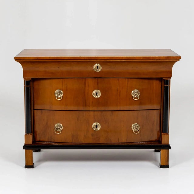 Biedermeier chest of drawers with cambered front and three drawers. The two lower drawers are flanked by ebonized columns....