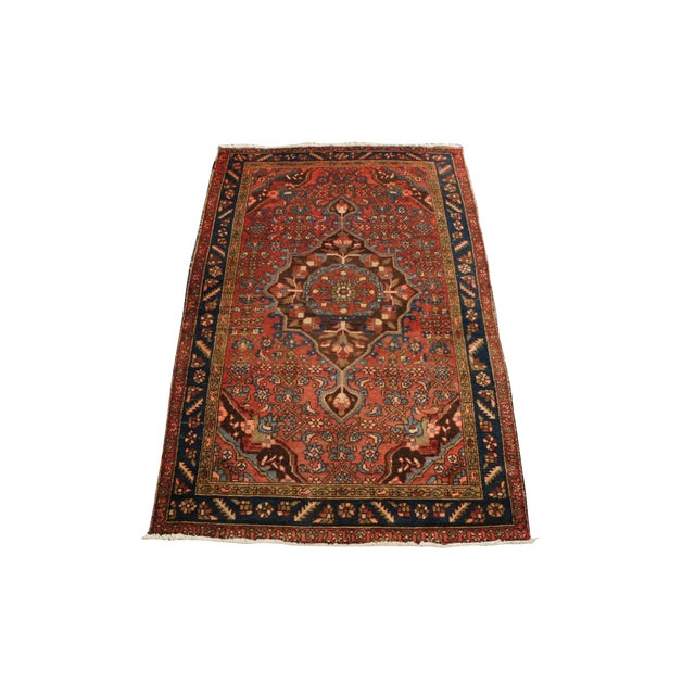 Hand-knotted area rug features a prominent, multi-layered geometric central medallion that anchors a vibrant rust-red...