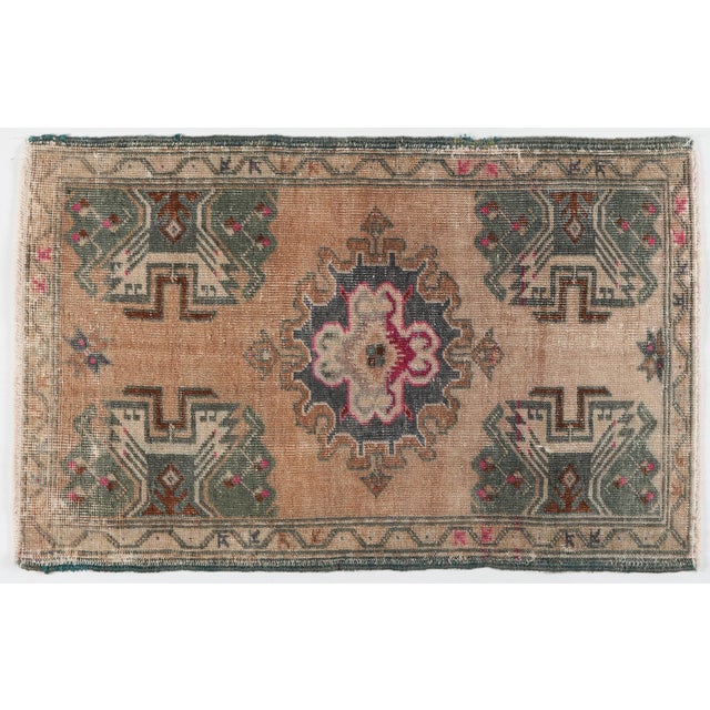 A vintage Turkish handwoven door mat rug featuring a bold geometric medallion and tribal motifs. Softly faded blush, sand,...