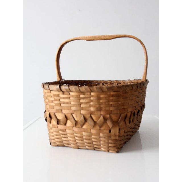 Antique handmade splint basket with a warm honey-toned surface, decorative woven diamond band, and bentwood handle....