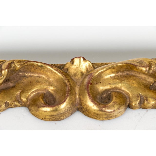 A small ornate carved gilt wood Baroque style wall mirror with a rich gold finish, deeply carved foliate motif, dense...