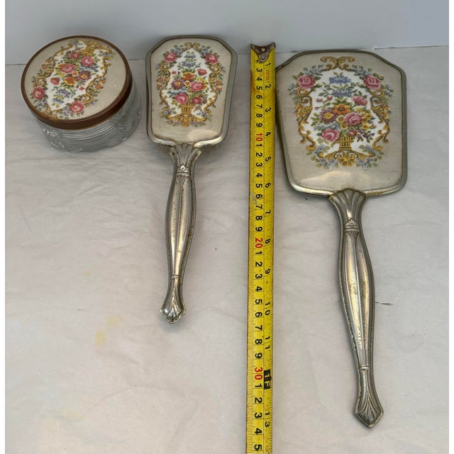 A charming mid-20th century vanity ensemble featuring a silver-plated hand mirror, matching hair brush, and coordinating...