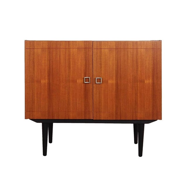 The cabinet was made in the 1970s in Denmark. The structure is covered with teak veneer. The legs are made of solid wood...