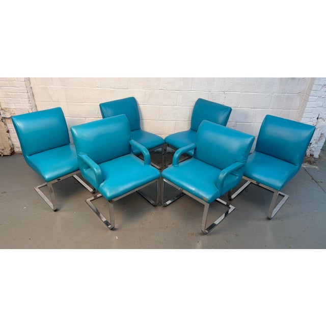 This set of six vintage mid-century dining chairs features striking blue vinyl upholstery with classic flat bar chrome...
