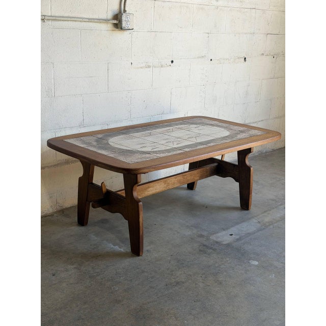 This rectangular coffee table features an inlaid ceramic tile top supported by a sturdy trestle base. Its clean geometric...