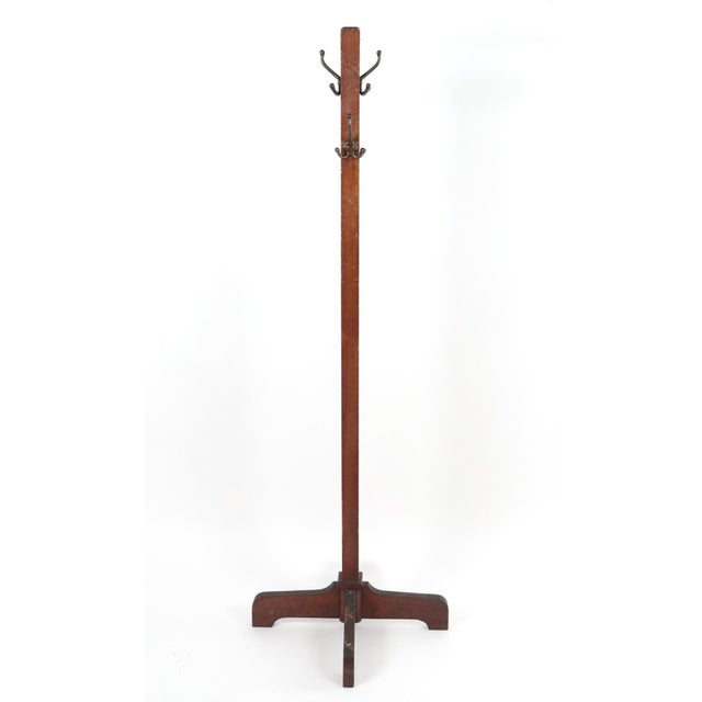Oak coat tree with a geometric design grounded by a quadripod base. There are four large triple hooks arranged at the top...