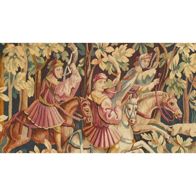 This antique French tapestry, woven in wool and silk, depicts a lively hunting scene set within a richly detailed forest...
