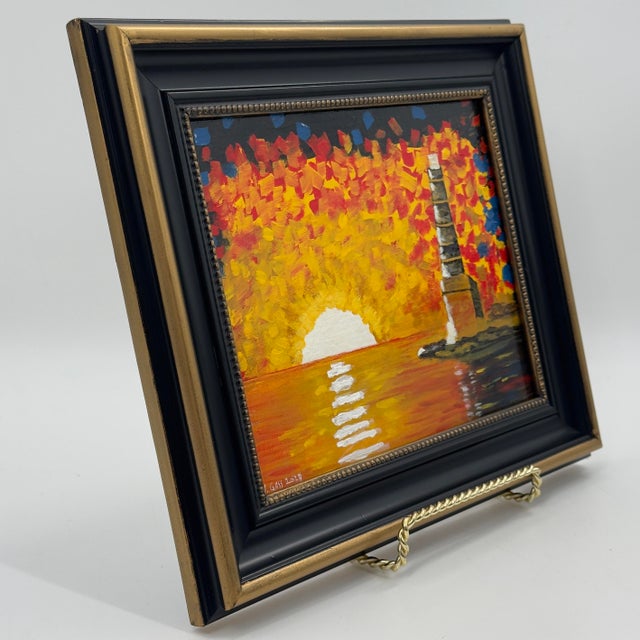 Original lighthouse painting on canvas board, depicting a striking coastal scene illuminated by a brilliant golden sunset....