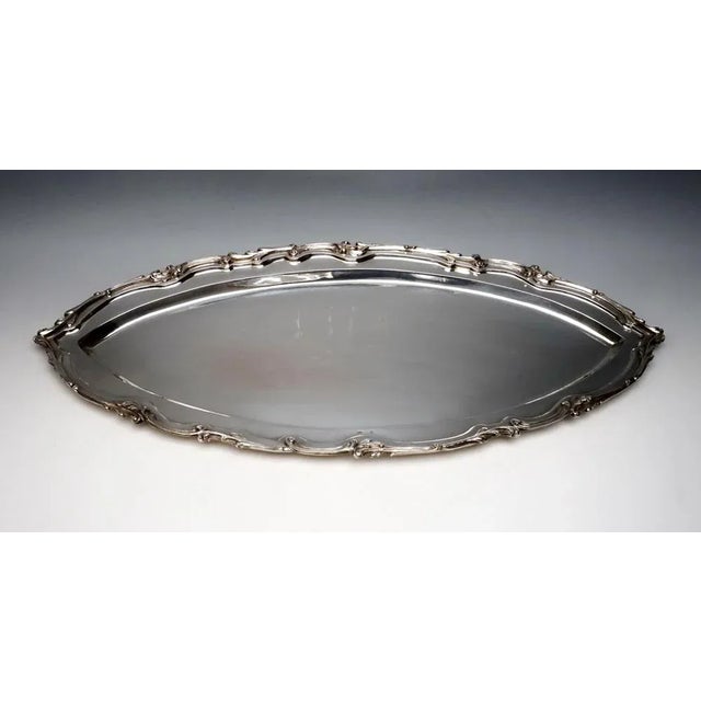 Large silver plate shaped like a boat in a smooth, simple design with a three-dimensional rocaille band on the edge of the...
