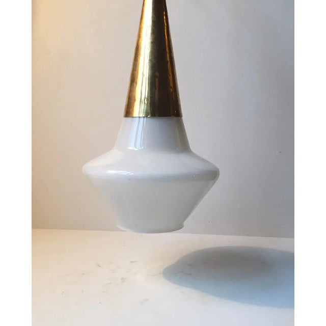 This Scandinavian pendant light is made of white opaline glass and is topped with a brass cone. It was manufactured and...