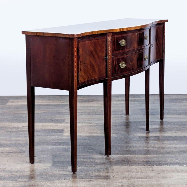 Mahogany serpentine sideboard with inlaid satinwood, two drawers, brass hardware, and felt lining for silverware. Brand:...