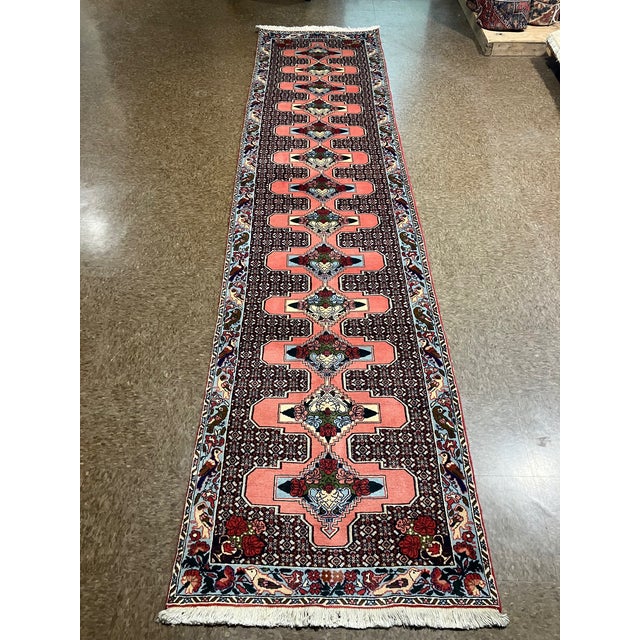 Hand-knotted Persian Kurdish wool runner featuring an elongated field with a repeating central medallion chain set on a...