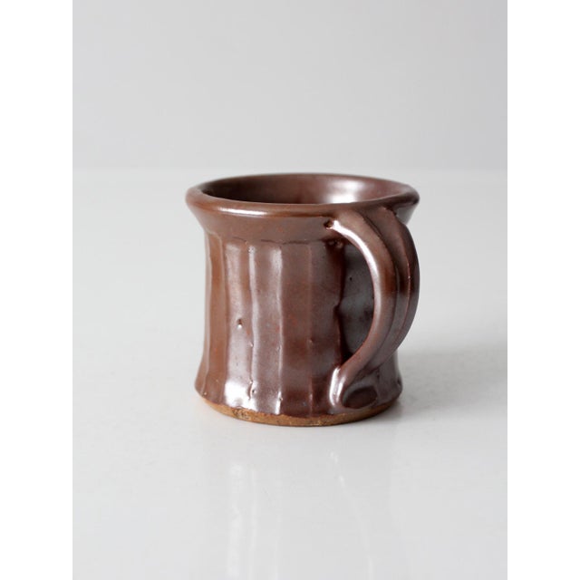 A vintage handmade studio pottery mug finished in a rich chocolate brown glaze with a soft metallic sheen. Its gently...