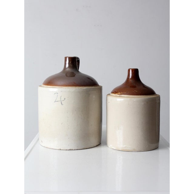 This pair of antique stoneware crocks features classic utilitarian forms with aged surfaces and warm, earthy tones. One...