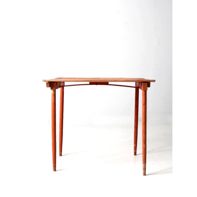 This is an antique "clipper" style folding table. Painted orange with black accents on the table top, the wooden side...