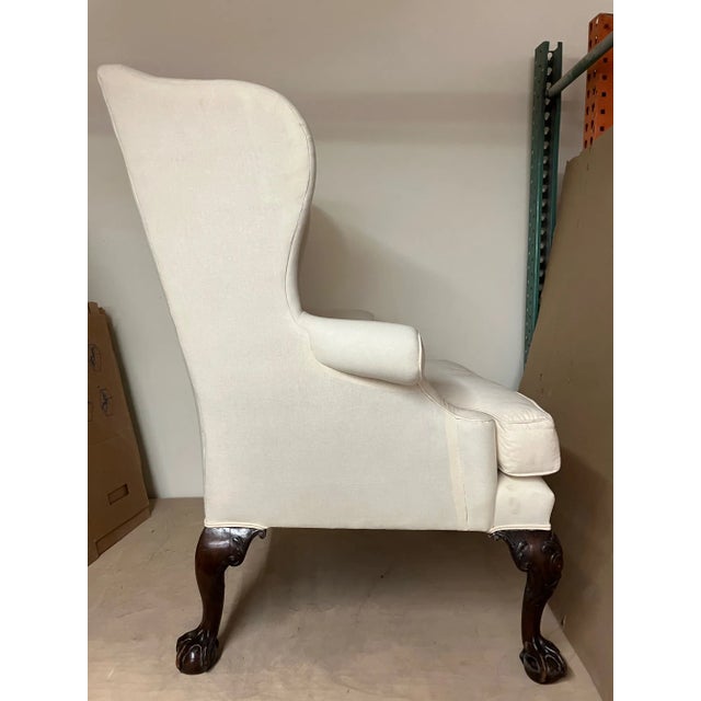 An antique Georgian winged armchair. It has been reupholstered in muslin. It has intricately carved claw feet made from...
