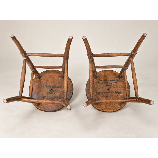 Pair of antique wooden stools with round solid wood seats, slender splayed legs, turned detailing, and stretcher supports....