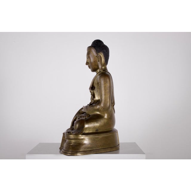 This inscribed and dated bronze Burmese Buddha from the Mandalay period depicts Shakyamuni in bhumisparsha mudra, the...