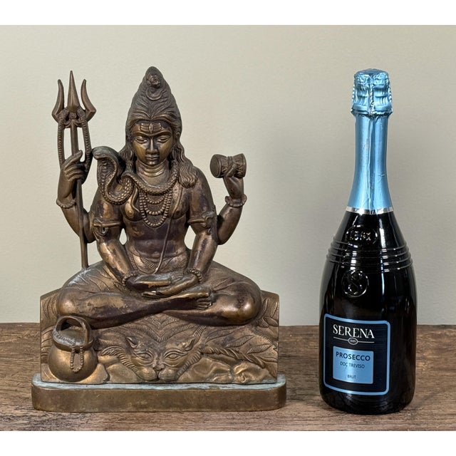 This heavy cast brass or bronze sculpture depicts the Hindu god Shiva seated in meditative posture holding a trident and...
