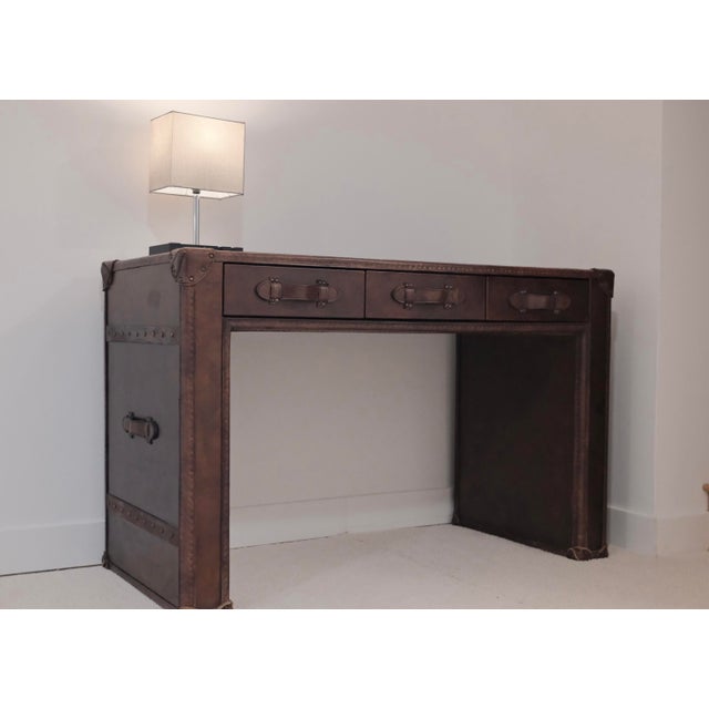 The Steamer Trunk Desk has a handmade solid wood frame wrapped in Vintage Cigar leather accented with up to 3,000 hand-...