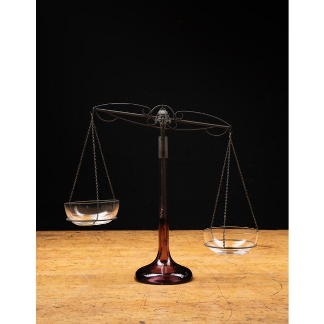 Early 20th-century apothecary balance scale featuring an amber glass pedestal base supporting an ornamental metal balance...
