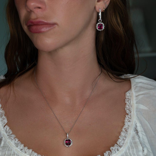 A rhodolite garnet glows in a rich raspberry-purple at the center of this solid 14K white gold pendant, framed by thirty-...