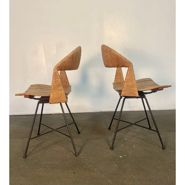 a nice pair of swiveling side chairs with black iron bases, slatted wood seats and rush backs. Designed By Arthur Umanoff....