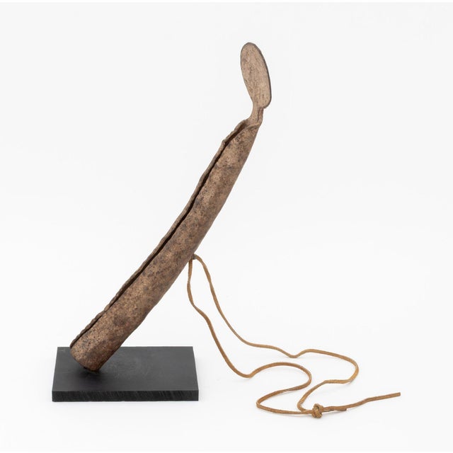 West African Senufo Hand-Forged Iron Rasp Gong, with tan leather strap mounted on ebonized wood base. Overall: 14.25" H x...