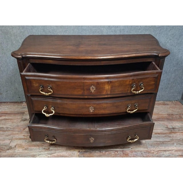 A Louis XV style bombé commode in solid walnut, mid-20th century. The serpentine front opens with three large molded...