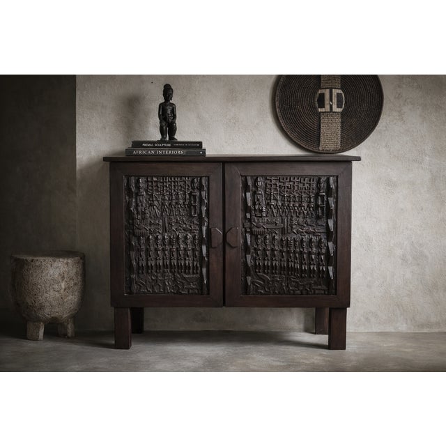 This sculptural wooden cabinet features two intricately carved panels inspired by traditional Dogon doors from Mali. Each...