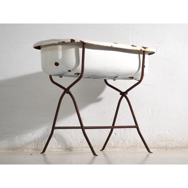 This antique bathtub in enamelled iron rests on a folding stand of bent iron tube. Originates from Central Europe, from...