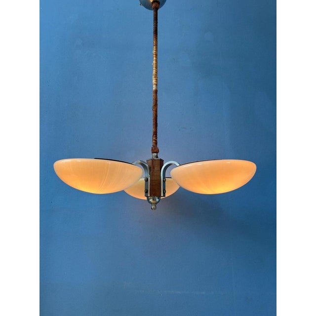 Original art deco light fixture with three glass shades. The shades are connected to a metal frame with wooden elements...