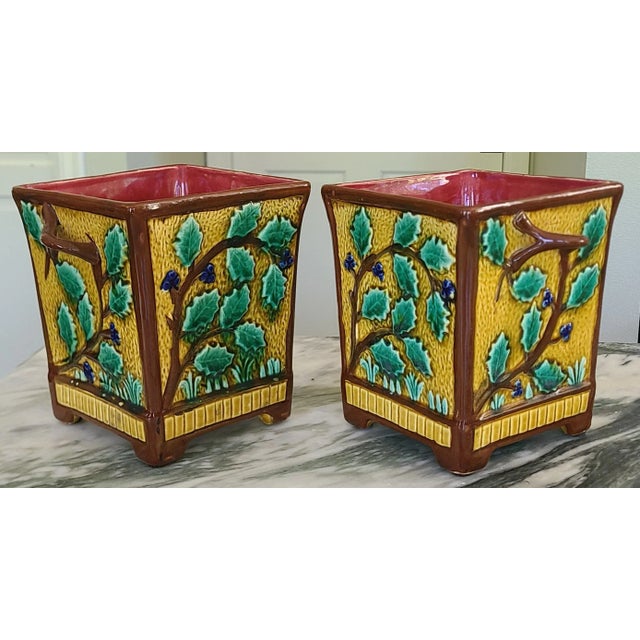 Presenting a pair of antique majolica cachepots in vibrant ocre, green, blue and brown exterior with a vibrant deep...