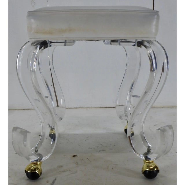 A modern era rolling stool on acrylic legs. The stool offers a white upholstered square seat set on ‘S’ shape acrylic legs...