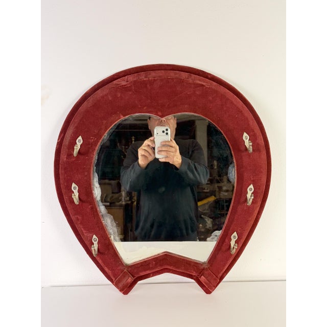 Red velvet horseshoe-shaped wall mirror, 1950s with coat hooks. Intact but with signs of age that testify to its...